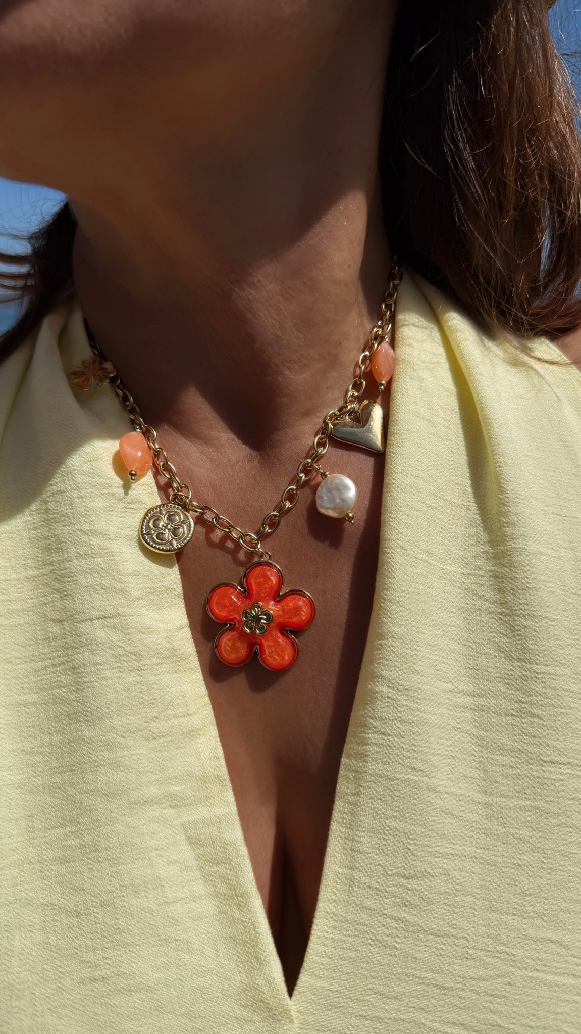 Collier chaîne dorée avec pendentif fleur corail, perle et charms colorés porté sur peau bronzée avec tenue estivale.