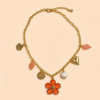 Collier chaîne dorée avec pendentif fleur corail, perle et charms colorés porté sur peau bronzée avec tenue estivale.
