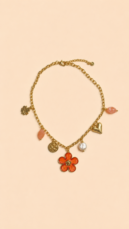Collier chaîne dorée avec pendentif fleur corail, perle et charms colorés porté sur peau bronzée avec tenue estivale.