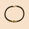 Collier en perles noires avec pendentif poisson doré porté autour du cou sur peau bronzée, look estival élégant.