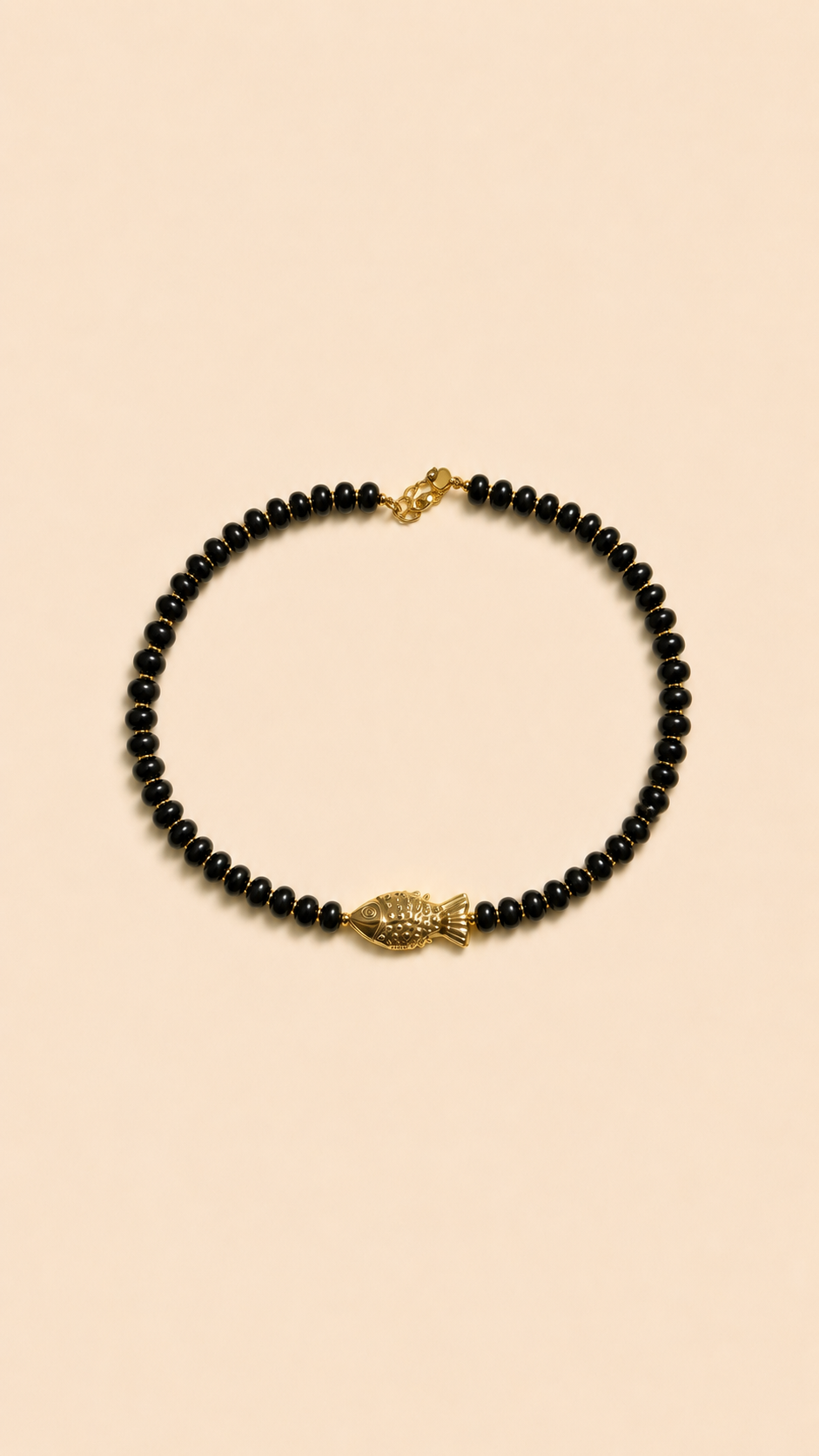 Collier en perles noires avec pendentif poisson doré porté autour du cou sur peau bronzée, look estival élégant.