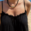 Collier en perles noires avec pendentif poisson doré porté autour du cou sur peau bronzée, look estival élégant.