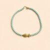 Collier en perles vert amande avec pendentif poisson doré porté autour du cou sur peau bronzée, look estival élégant.