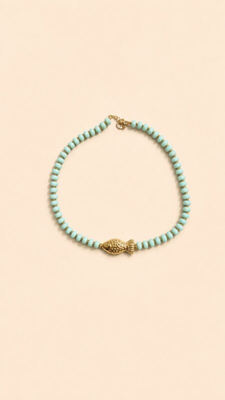 Collier en perles vert amande avec pendentif poisson doré porté autour du cou sur peau bronzée, look estival élégant.