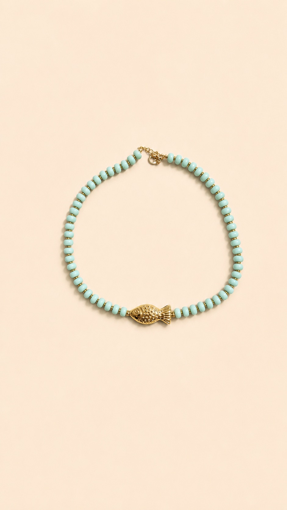 Collier en perles vert amande avec pendentif poisson doré porté autour du cou sur peau bronzée, look estival élégant.