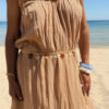 Femme portant deux bracelets rigides nacrés vert avec détails dorés en forme de soleil sur une plage ensoleillée, look élégant et estival
