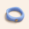 Femme portant deux bracelets rigides nacrés vert avec détails dorés en forme de soleil sur une plage ensoleillée, look élégant et estival