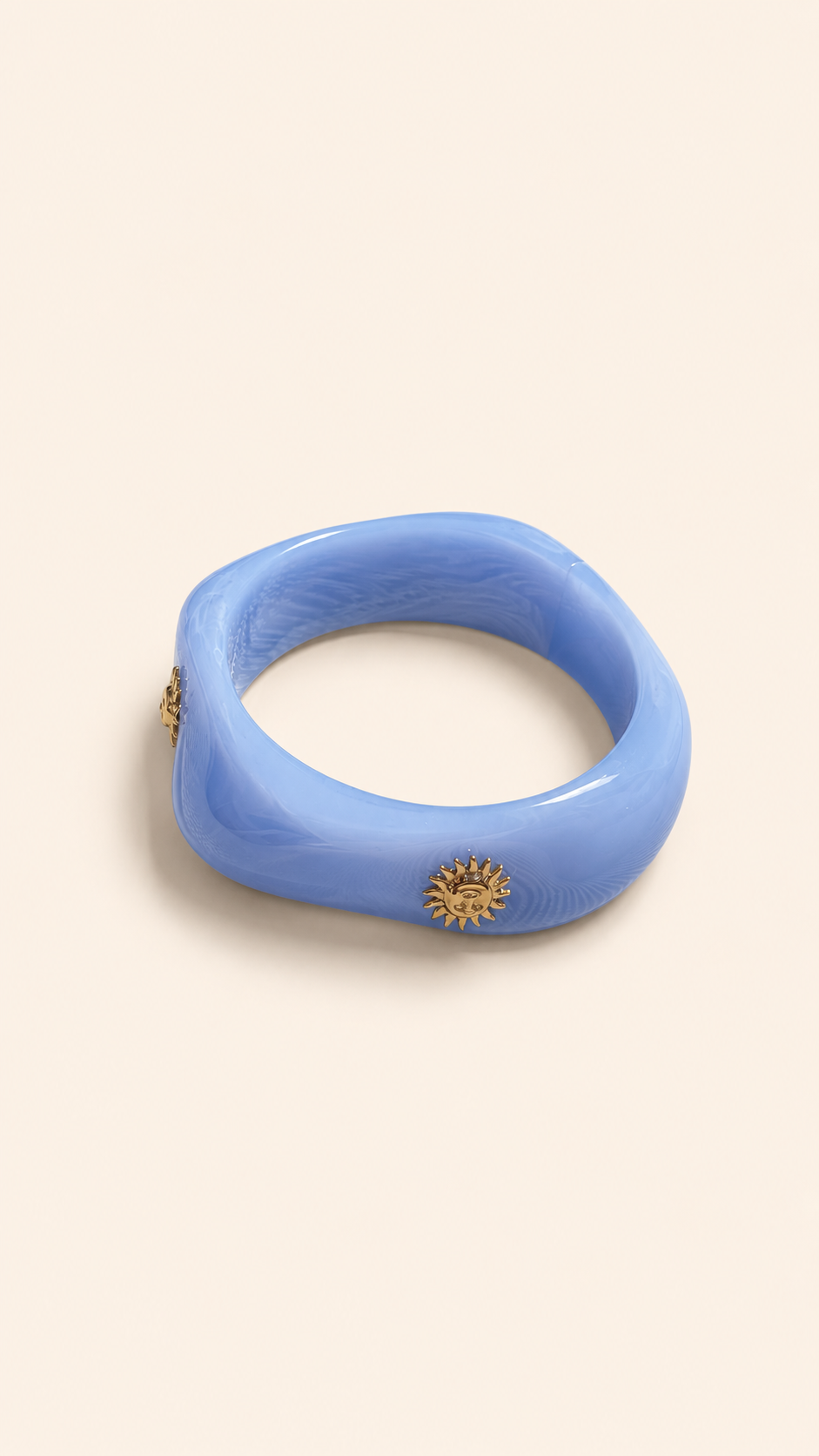 Femme portant deux bracelets rigides nacrés vert avec détails dorés en forme de soleil sur une plage ensoleillée, look élégant et estival