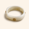 Femme portant deux bracelets rigides nacrés écrus avec détails dorés en forme de soleil sur une plage ensoleillée, look élégant et estival avec robe noire fluide.