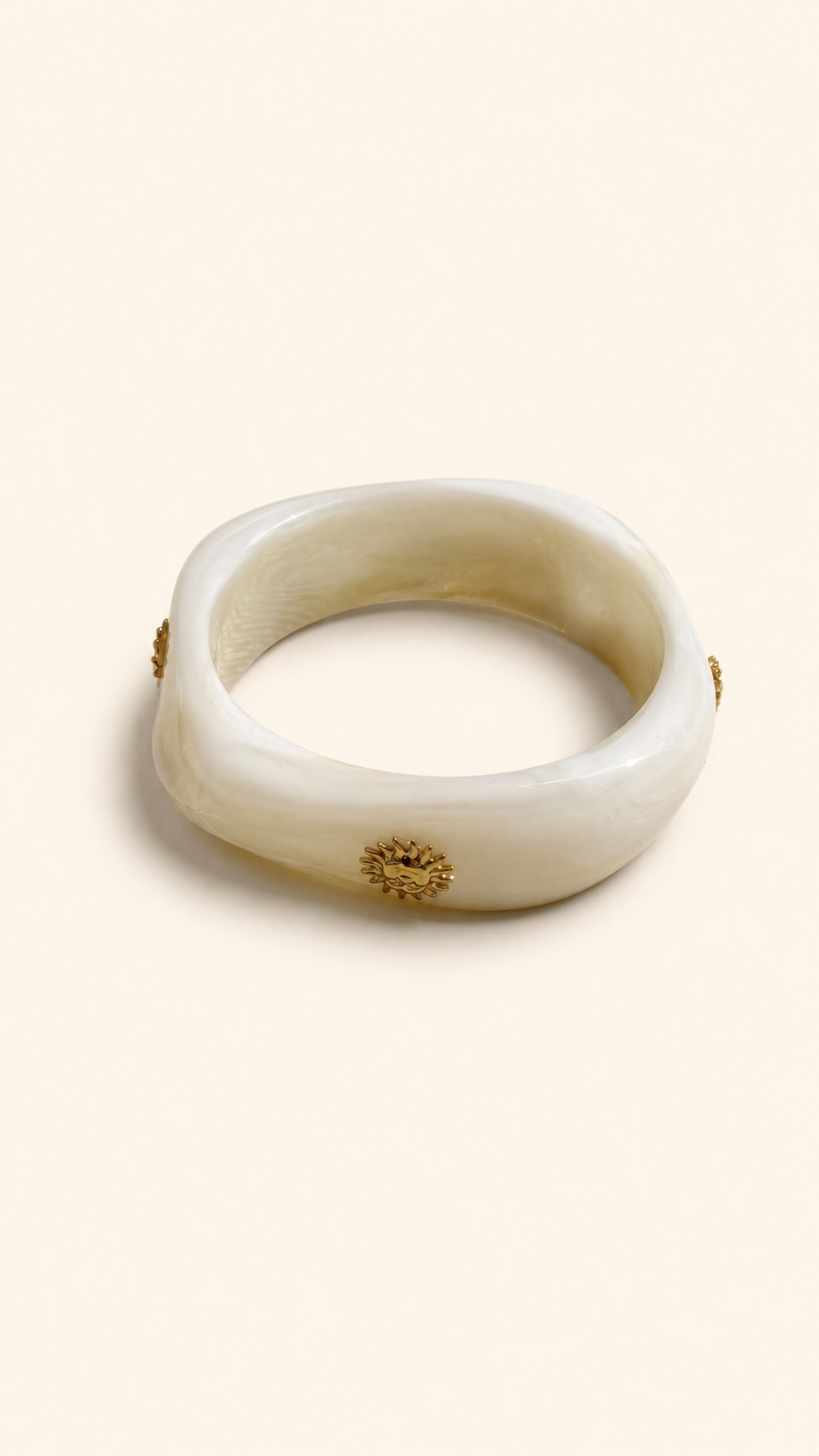 Femme portant deux bracelets rigides nacrés écrus avec détails dorés en forme de soleil sur une plage ensoleillée, look élégant et estival avec robe noire fluide.