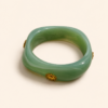 Femme portant deux bracelets rigides nacrés vert avec détails dorés en forme de soleil sur une plage ensoleillée, look élégant et estival