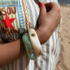Femme portant deux bracelets rigides nacrés vert avec détails dorés en forme de soleil sur une plage ensoleillée, look élégant et estival