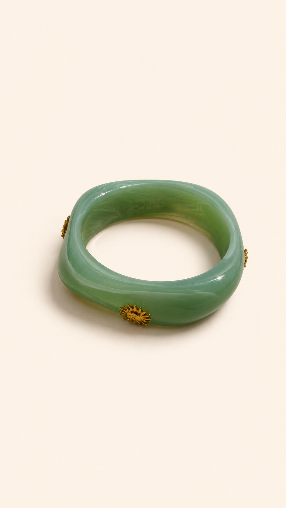 Femme portant deux bracelets rigides nacrés vert avec détails dorés en forme de soleil sur une plage ensoleillée, look élégant et estival