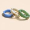 Femme portant deux bracelets rigides nacrés écrus avec détails dorés en forme de soleil sur une plage ensoleillée, look élégant et estival avec robe noire fluide.