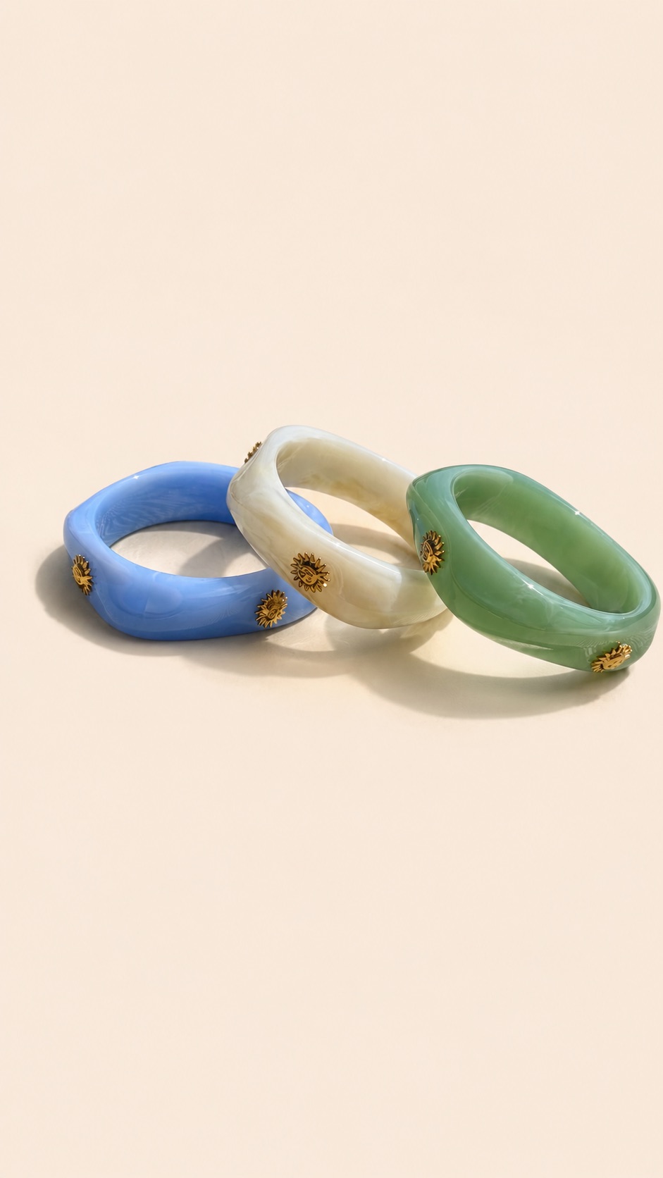 Femme portant deux bracelets rigides nacrés écrus avec détails dorés en forme de soleil sur une plage ensoleillée, look élégant et estival avec robe noire fluide.
