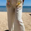 Femme portant l'ensemble Zoé composé d'une blouse rayée vert brodée et d'un pantalon fluide rayé vert sur une plage ensoleillée.