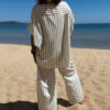 Femme portant l'ensemble Zoé composé d'une blouse rayée vert brodée et d'un pantalon fluide rayé vert sur une plage ensoleillée.