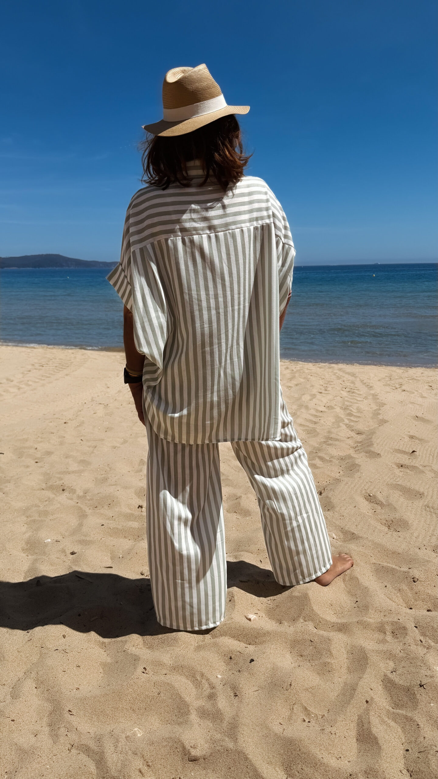 Femme portant l'ensemble Zoé composé d'une blouse rayée vert brodée et d'un pantalon fluide rayé vert sur une plage ensoleillée.