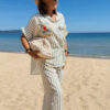 Femme portant l'ensemble Zoé composé d'une blouse rayée vert brodée et d'un pantalon fluide rayé vert sur une plage ensoleillée.