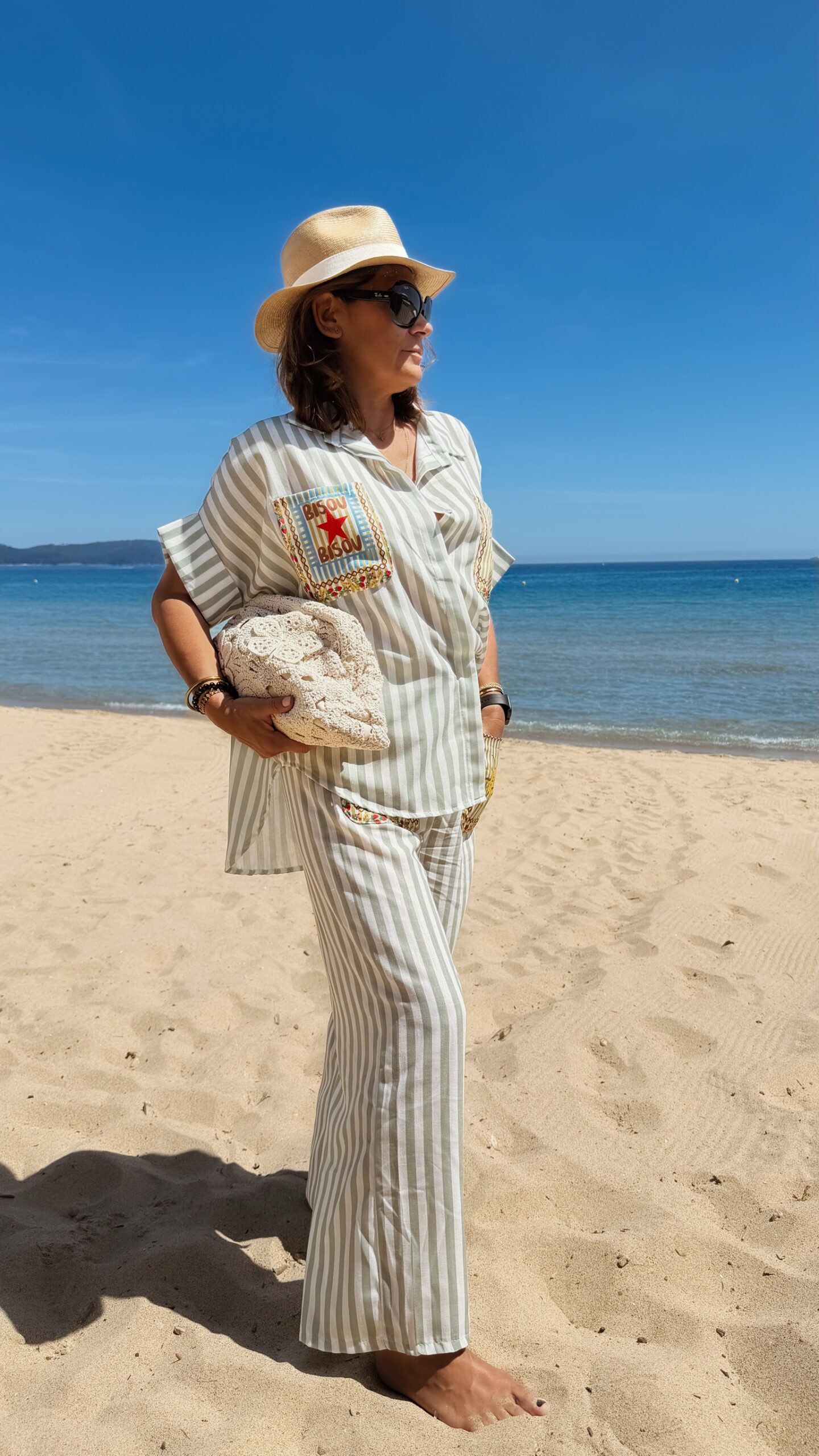 Femme portant l'ensemble Zoé composé d'une blouse rayée vert brodée et d'un pantalon fluide rayé vert sur une plage ensoleillée.