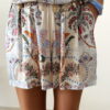 short femme bohème chic bleu à motif cachemire composé d'une chemise fluide et d'un short léger, porté sur une plage en été.