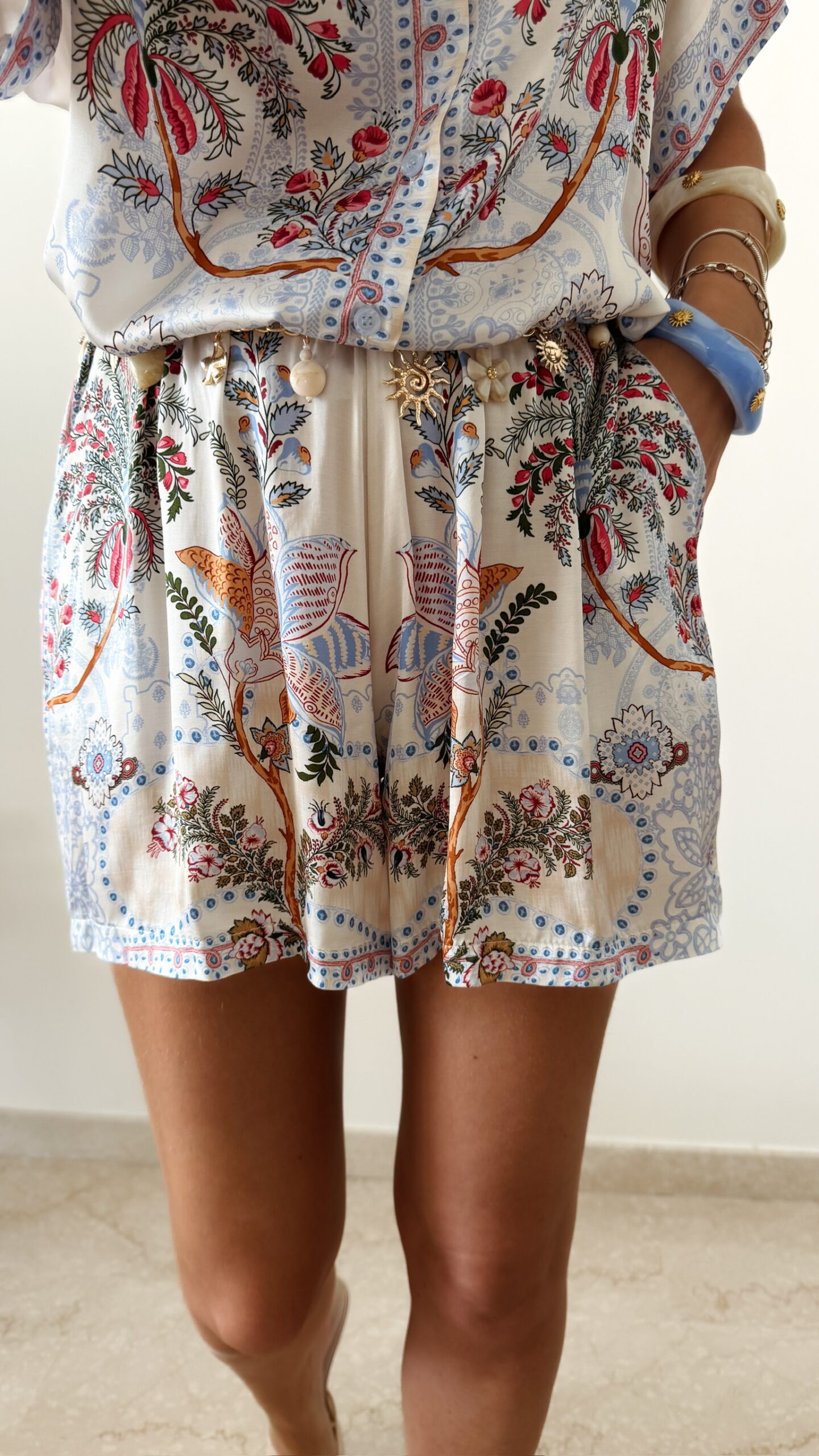 short femme bohème chic bleu à motif cachemire composé d'une chemise fluide et d'un short léger, porté sur une plage en été.