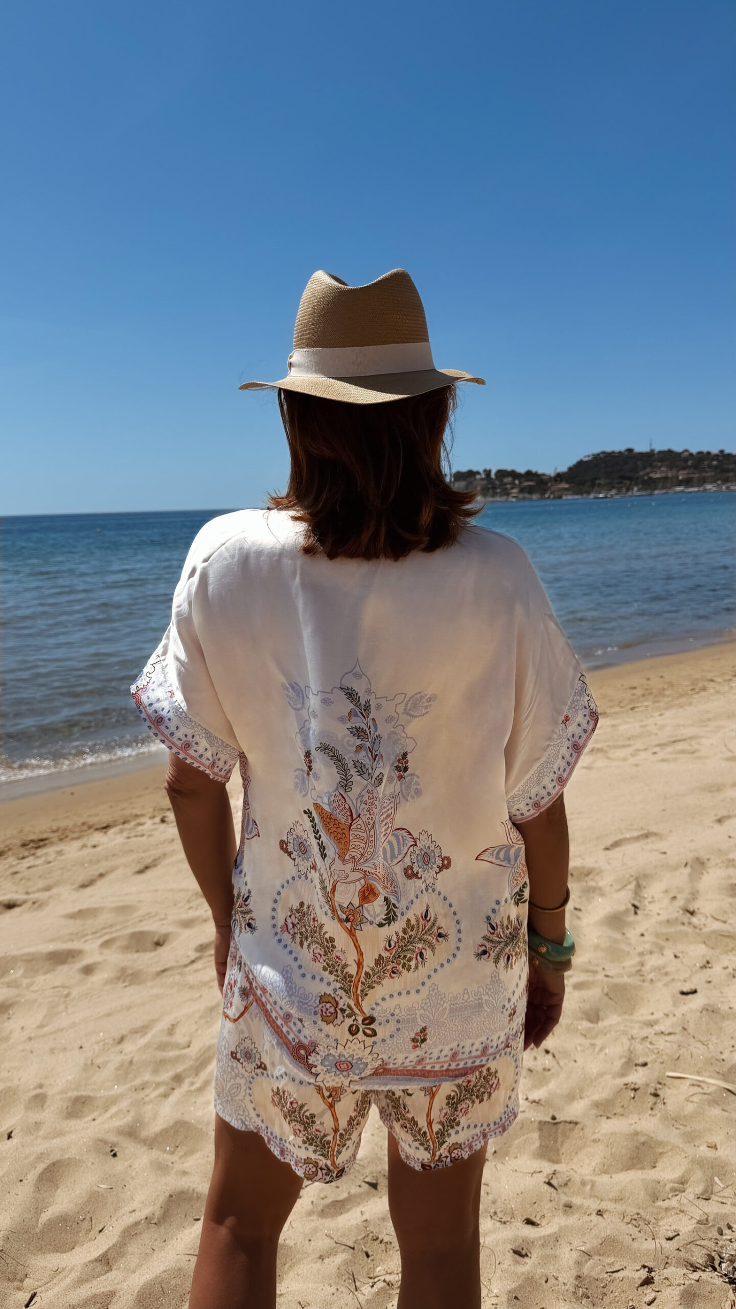 Ensemble femme bohème chic bleu à motif cachemire composé d'une chemise fluide et d'un short léger, porté sur une plage en été.