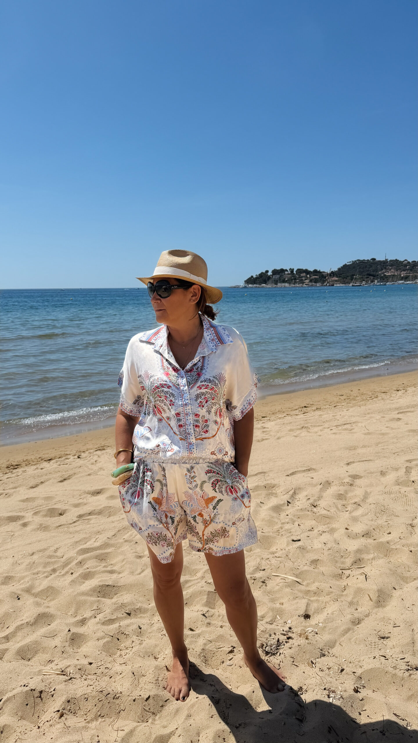 Ensemble femme bohème chic bleu à motif cachemire composé d'une chemise fluide et d'un short léger, porté sur une plage en été.