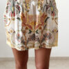 Ensemble femme bohème chic beige à motif cachemire composé d'une chemise fluide et d'un short léger, porté sur une plage en été.
