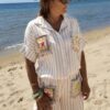 Femme portant l'ensemble Zoé composé d'une blouse rayée beige brodée et d'un pantalon fluide rayé beige sur une plage ensoleillée.
