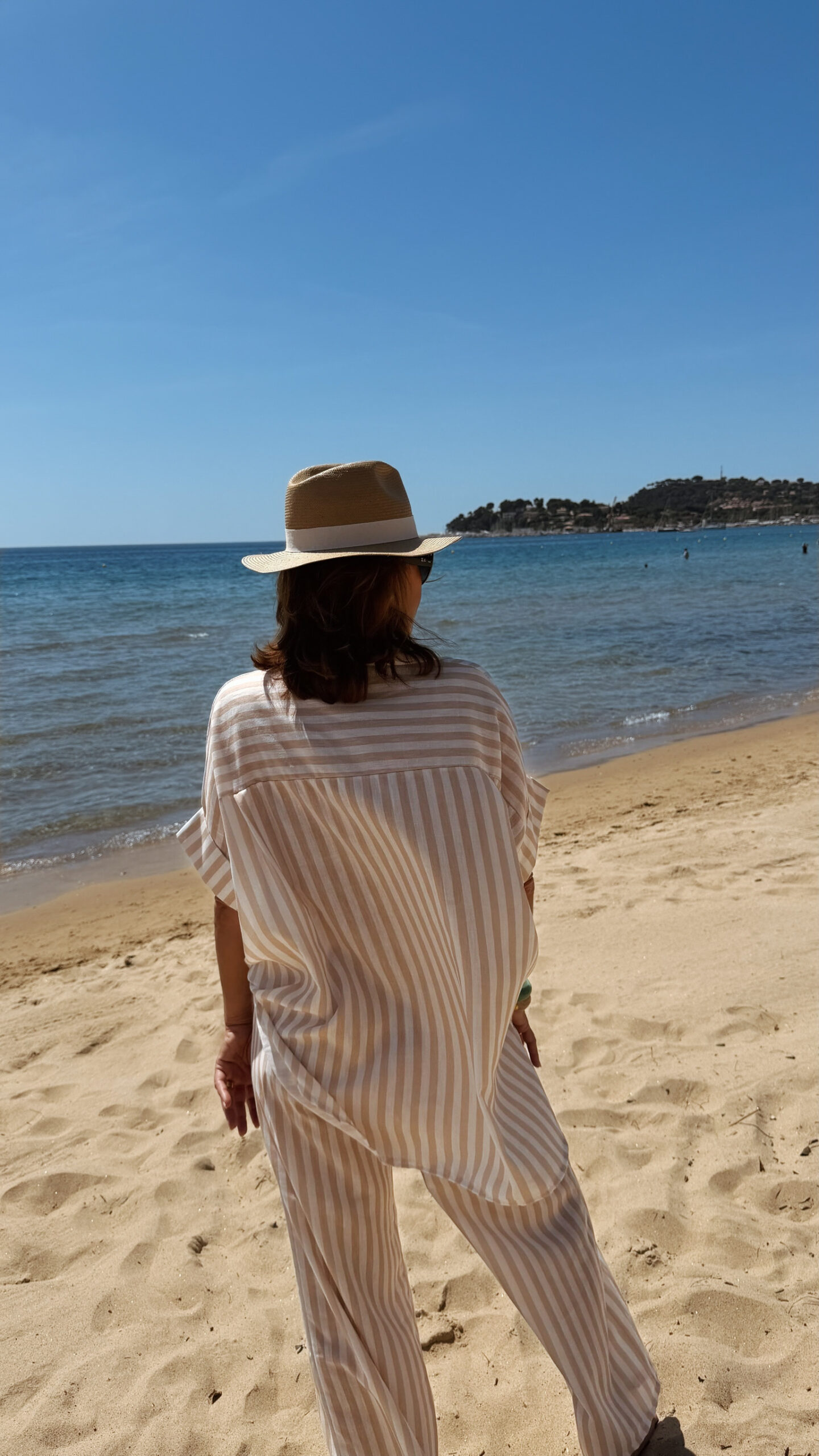 Femme portant l'ensemble Zoé composé d'une blouse rayée beige brodée et d'un pantalon fluide rayé beige sur une plage ensoleillée.