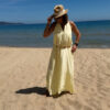 Robe longue jaune dos nu Carla pour femme, coupe fluide et élégante, portée sur une plage en bord de mer sous le soleil d'été.