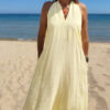 Robe longue jaune dos nu Carla pour femme, coupe fluide et élégante, portée sur une plage en bord de mer sous le soleil d'été.