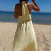 Robe longue jaune dos nu Carla pour femme, coupe fluide et élégante, portée sur une plage en bord de mer sous le soleil d'été.