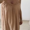 Femme portant une robe longue camel en gaze de coton sur une plage ensoleillée, avec chapeau et lunettes de soleil.
