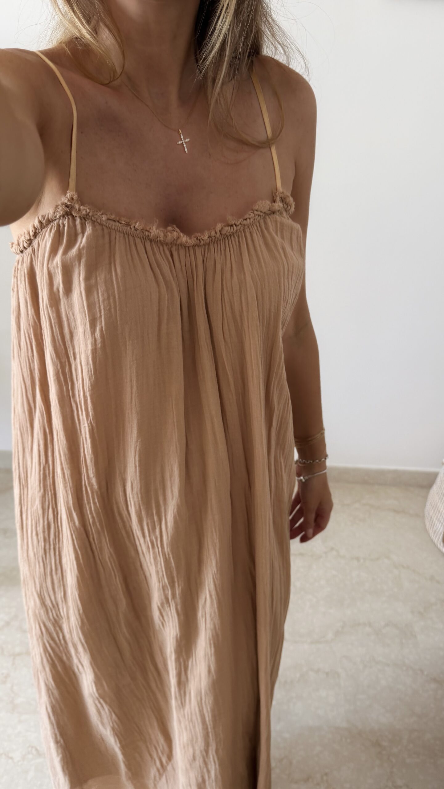 Femme portant une robe longue camel en gaze de coton sur une plage ensoleillée, avec chapeau et lunettes de soleil.