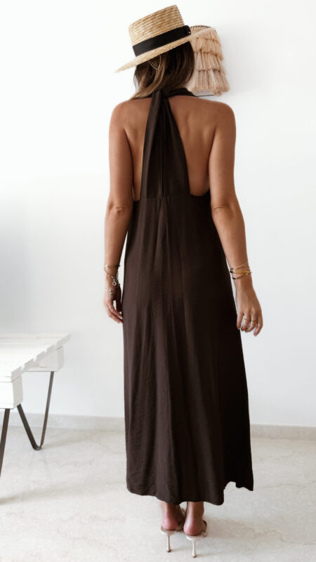 Robe longue marron dos nu Carla pour femme, coupe fluide et élégante, portée sur une plage en bord de mer sous le soleil d'été.