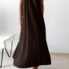 Robe longue marron dos nu Carla pour femme, coupe fluide et élégante, portée sur une plage en bord de mer sous le soleil d'été.