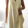 Robe longue jaune dos nu Carla pour femme, coupe fluide et élégante, portée sur une plage en bord de mer sous le soleil d'été.
