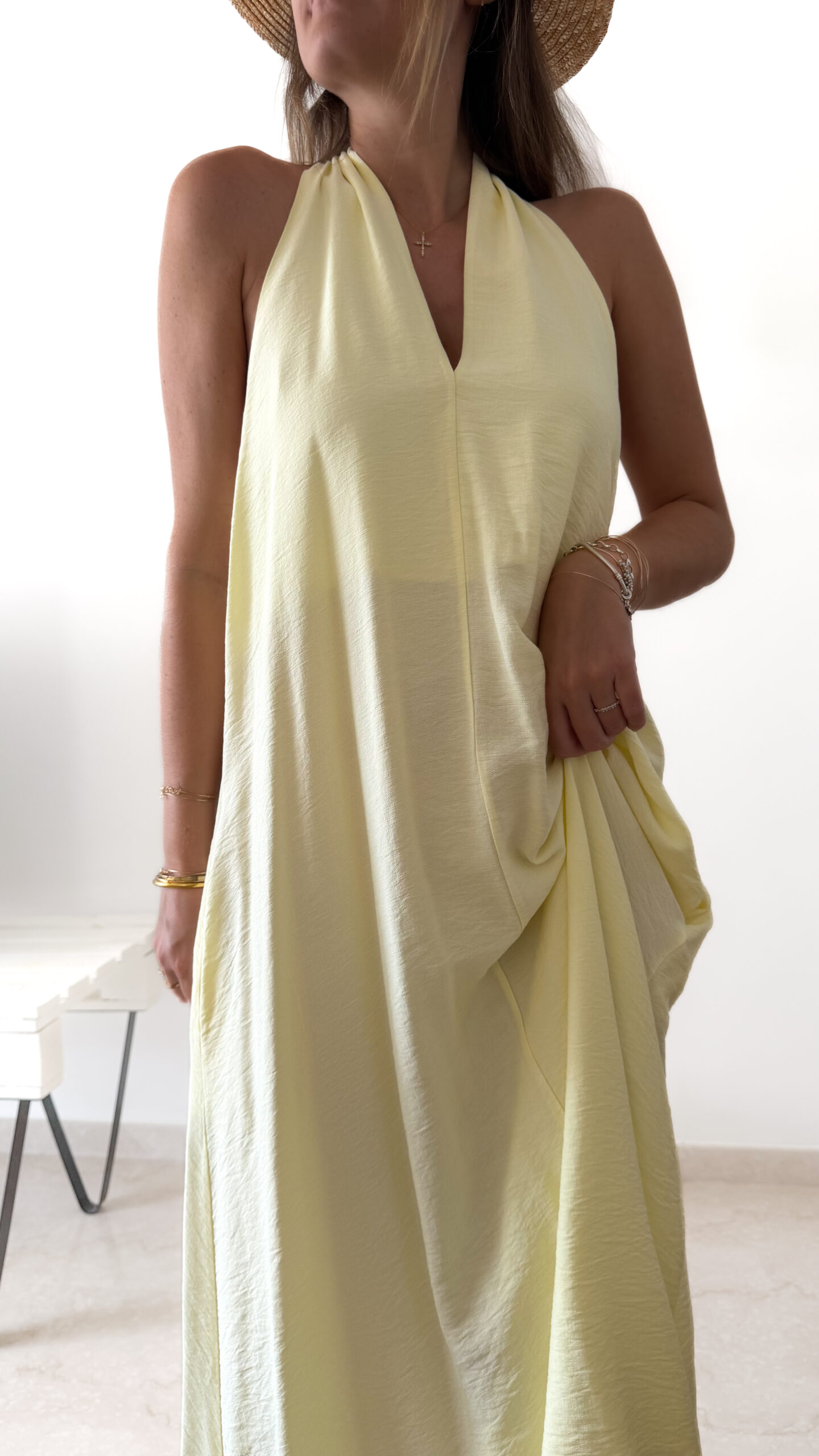 Robe longue jaune dos nu Carla pour femme, coupe fluide et élégante, portée sur une plage en bord de mer sous le soleil d'été.