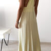 Robe longue jaune dos nu Carla pour femme, coupe fluide et élégante, portée sur une plage en bord de mer sous le soleil d'été.