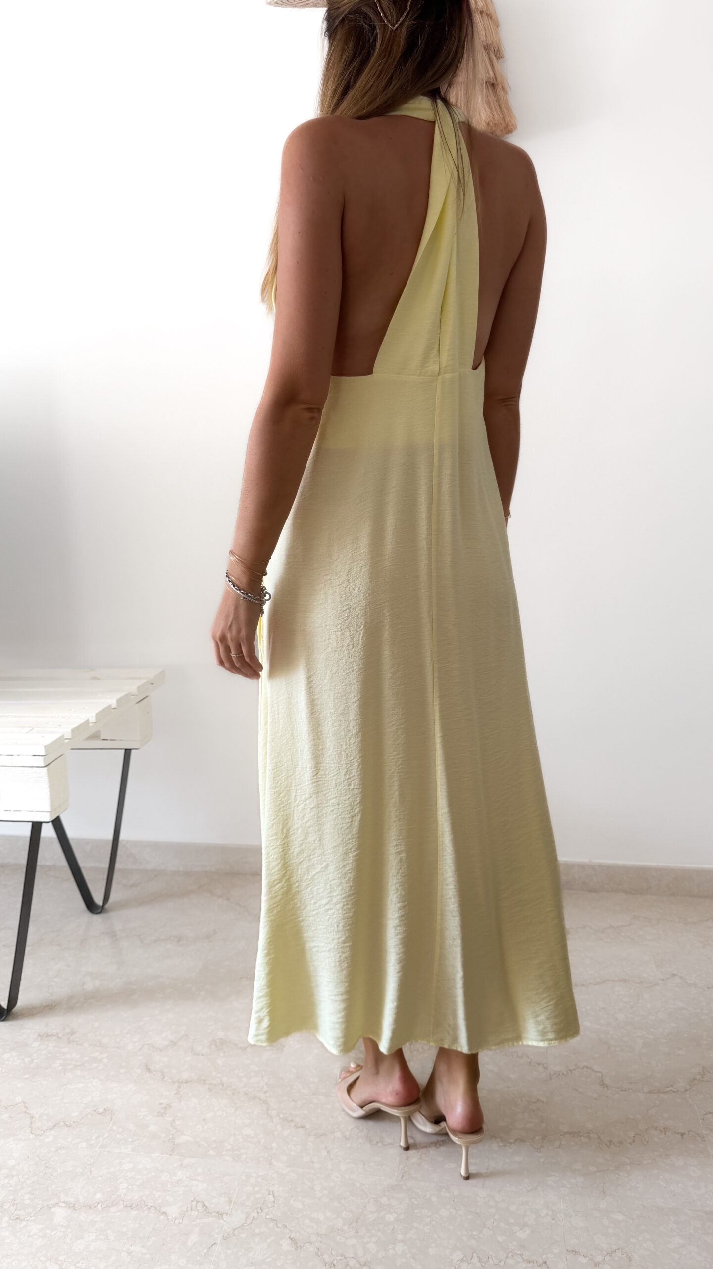 Robe longue jaune dos nu Carla pour femme, coupe fluide et élégante, portée sur une plage en bord de mer sous le soleil d'été.
