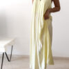 Robe longue jaune dos nu Carla pour femme, coupe fluide et élégante, portée sur une plage en bord de mer sous le soleil d'été.