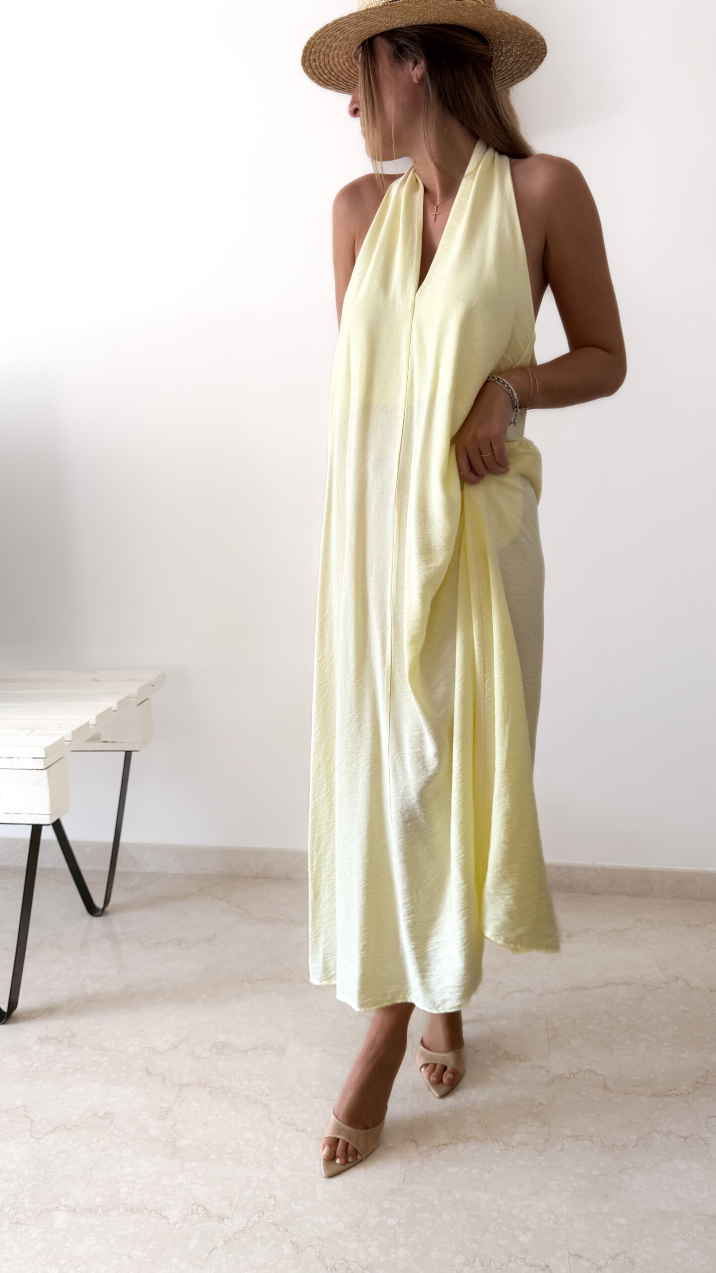 Robe longue jaune dos nu Carla pour femme, coupe fluide et élégante, portée sur une plage en bord de mer sous le soleil d'été.
