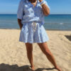 Ensemble Ninon femme bleu ciel et blanc brodé, composé d'une blouse légère et d'un short assorti, porté sur une plage en été.