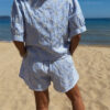 Ensemble Ninon femme bleu ciel et blanc brodé, composé d'une blouse légère et d'un short assorti, porté sur une plage en été.