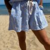 Ensemble Ninon femme bleu ciel et blanc brodé, composé d'une blouse légère et d'un short assorti, porté sur une plage en été.