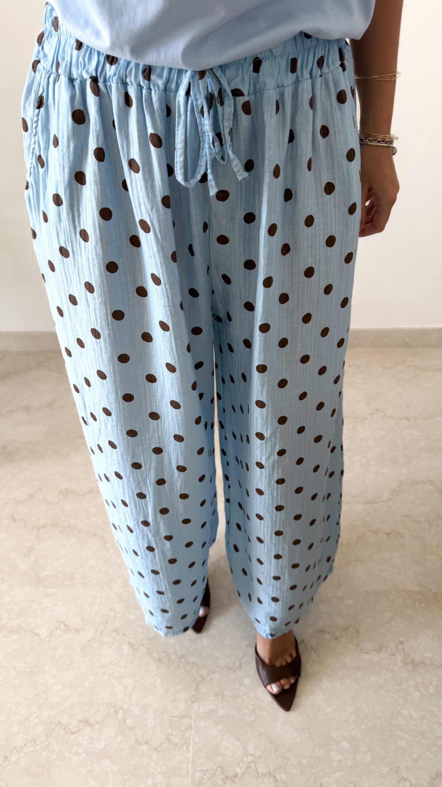 Femme portant un pantalon bleu ciel à pois marron avec taille élastique et lien de serrage, associé à un haut uni.