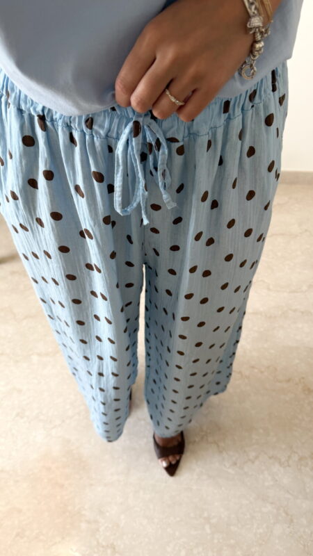 Femme portant un pantalon bleu ciel à pois marron avec taille élastique et lien de serrage, associé à un haut uni.