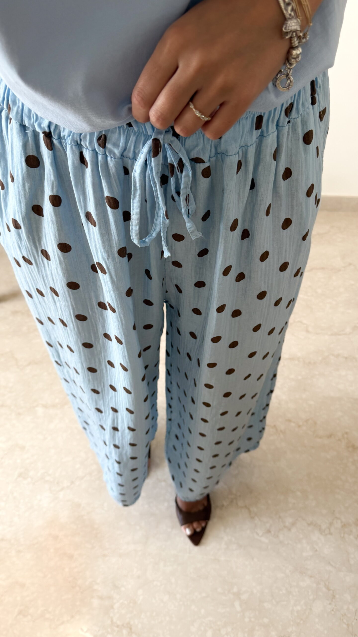 Femme portant un pantalon bleu ciel à pois marron avec taille élastique et lien de serrage, associé à un haut uni.
